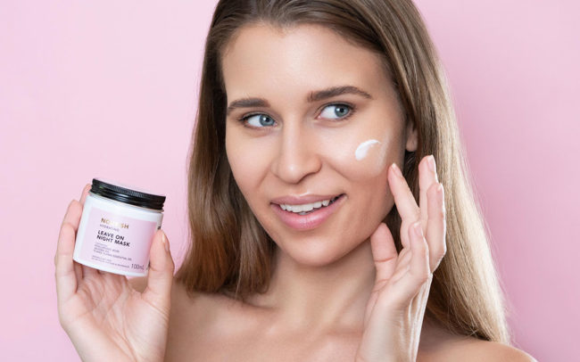 amy rose hancock woman holding skincare product on pink background